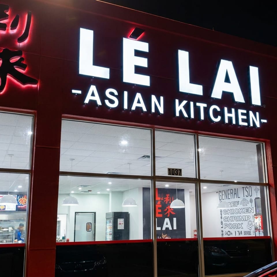Le Lai Asian Kitchen restaurant storefront illuminated at night, with red signage, large windows, and menu boards visible inside.