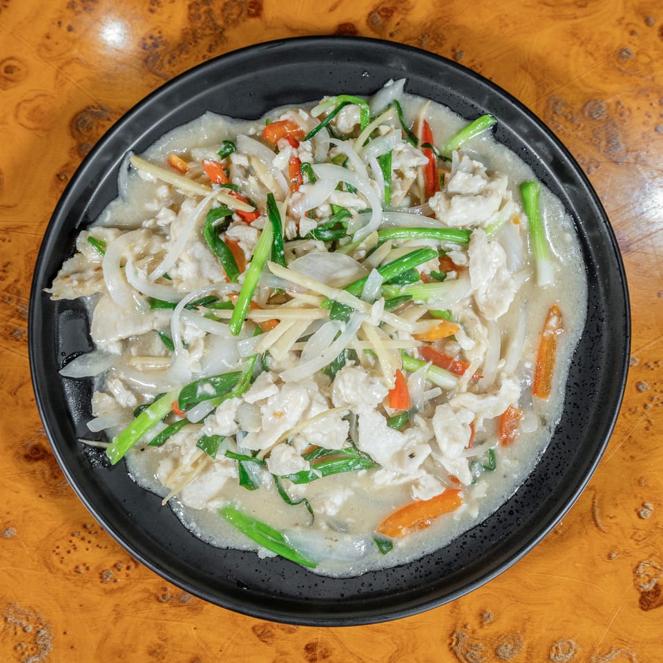 Chicken stir-fry with onions, carrots, peppers, and green onions in a light sauce, served on a black plate.