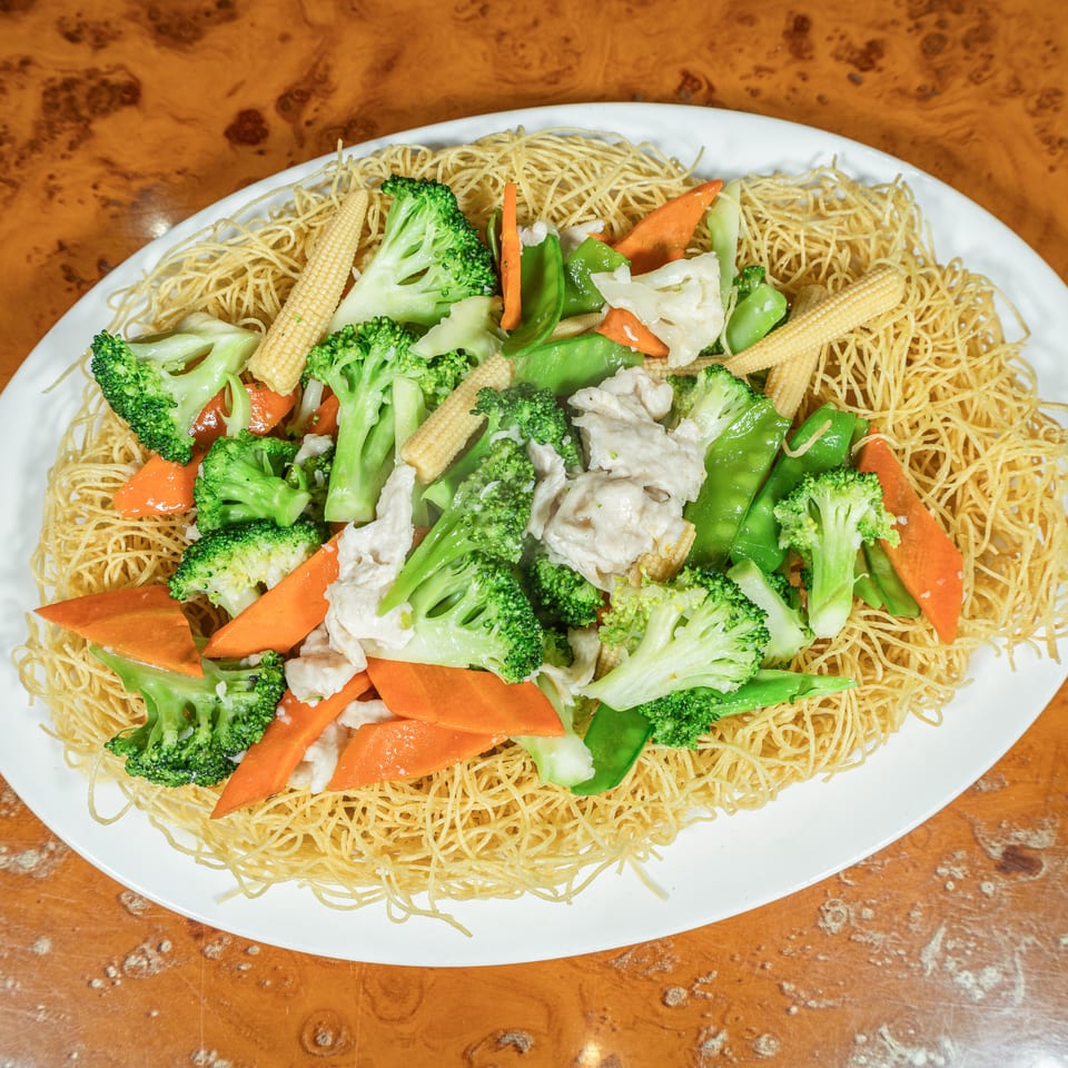 Crispy noodles topped with chicken and colorful stir-fried vegetables on a white oval plate.